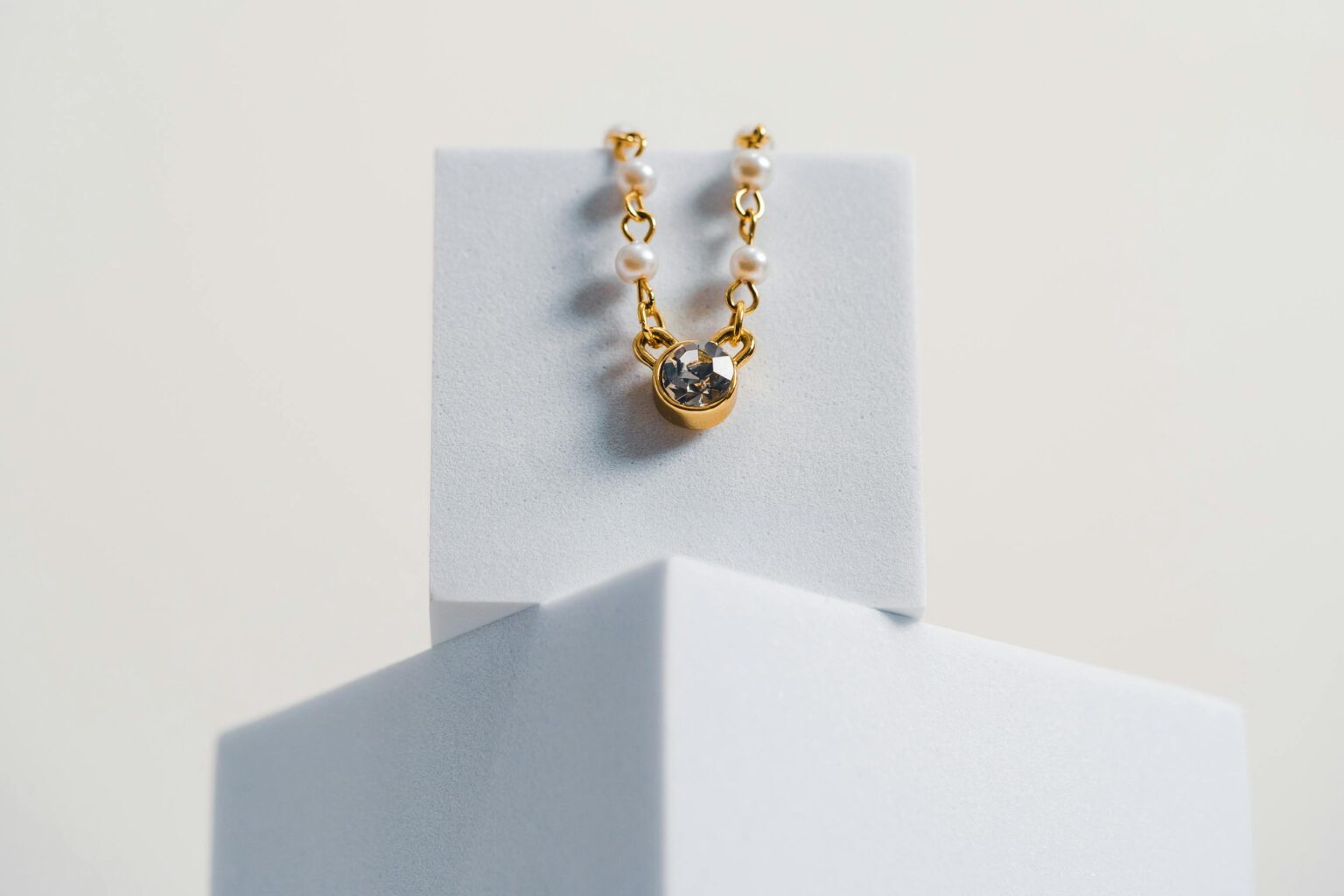 Minimalist photo of a gold necklace with pearls and a gemstone on a white geometric stand.